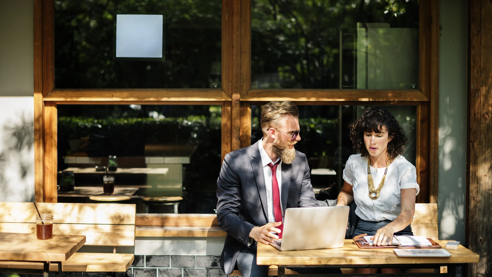 Two professionals discussing documents beside a laptop at a cafe table.