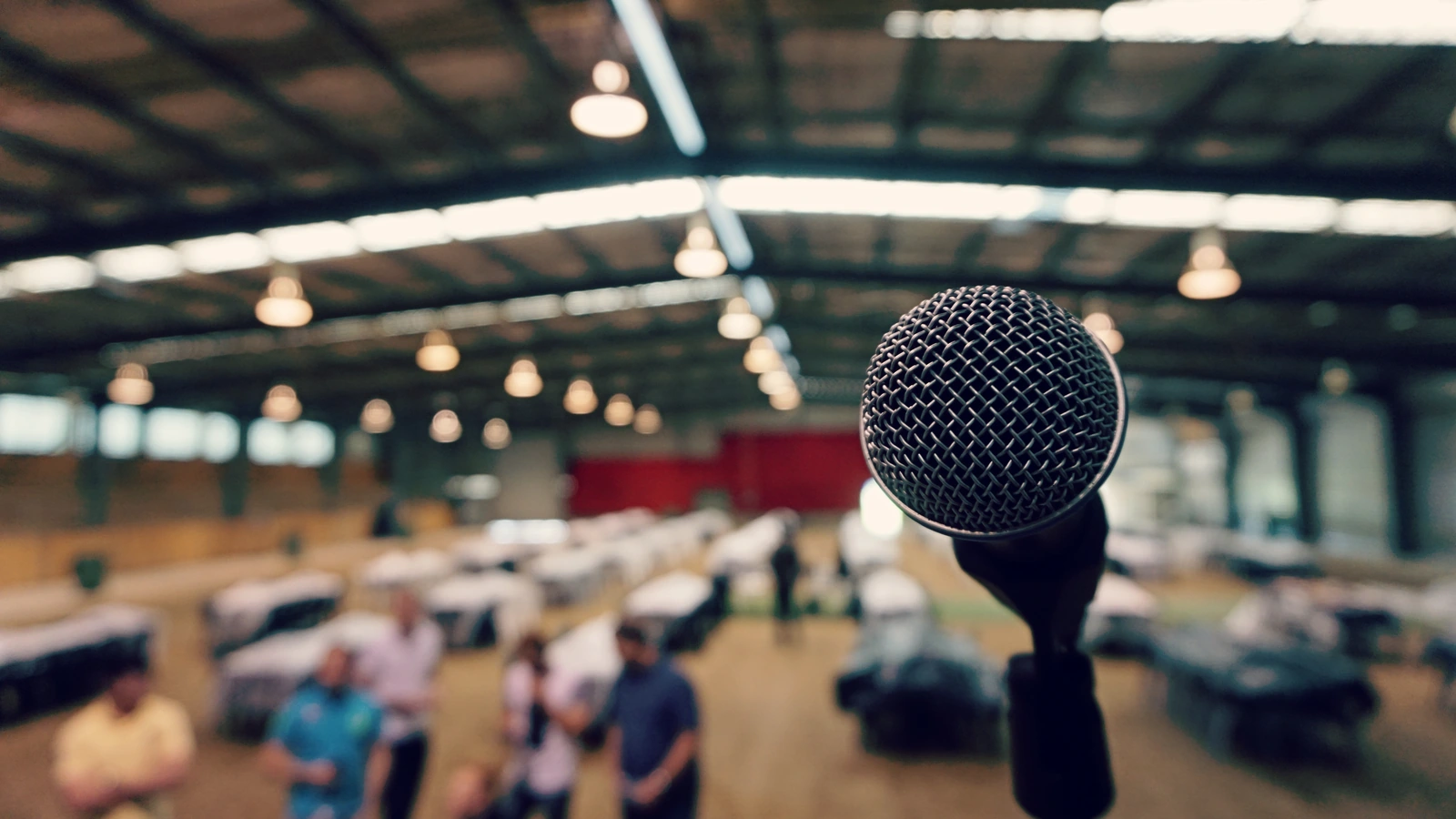 Microphone in sharp focus with people and tables blurred in the background of a large hall.