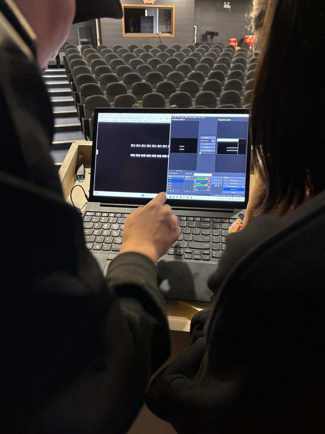 Two people checking a laptop-based caption display setup inside the Britannica Shanghai auditorium.