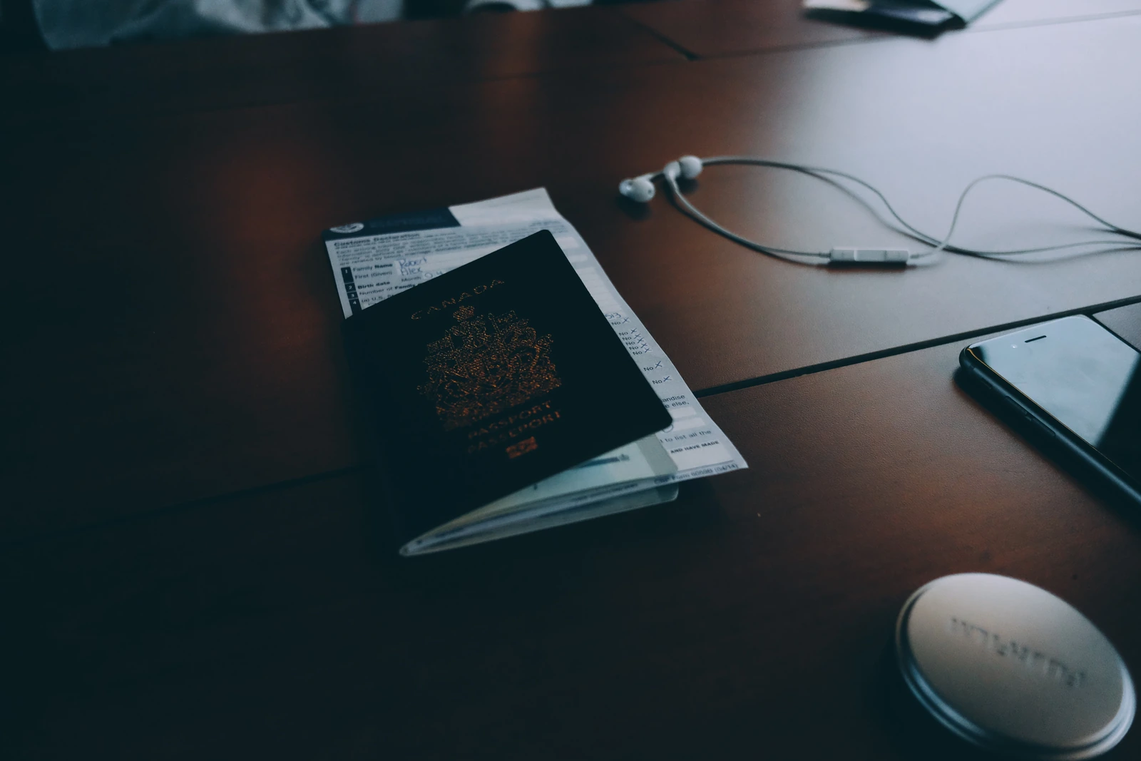 Canadian passport and travel documents on a desk beside a phone and earphones.